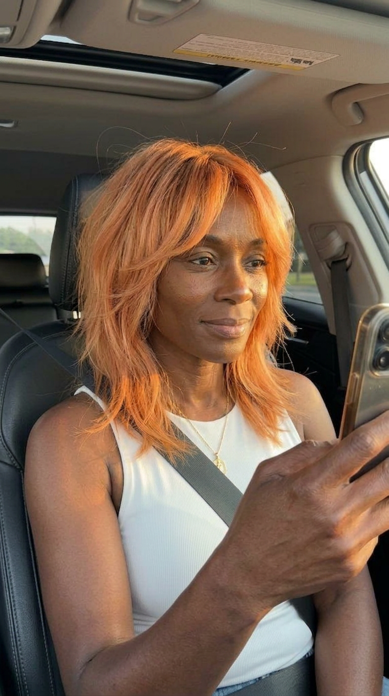 Vivid copper layered shag haircut with airy movement, soft fringe, and sunlit car-selfie mood for a bold summer 2026 refresh for women over 40