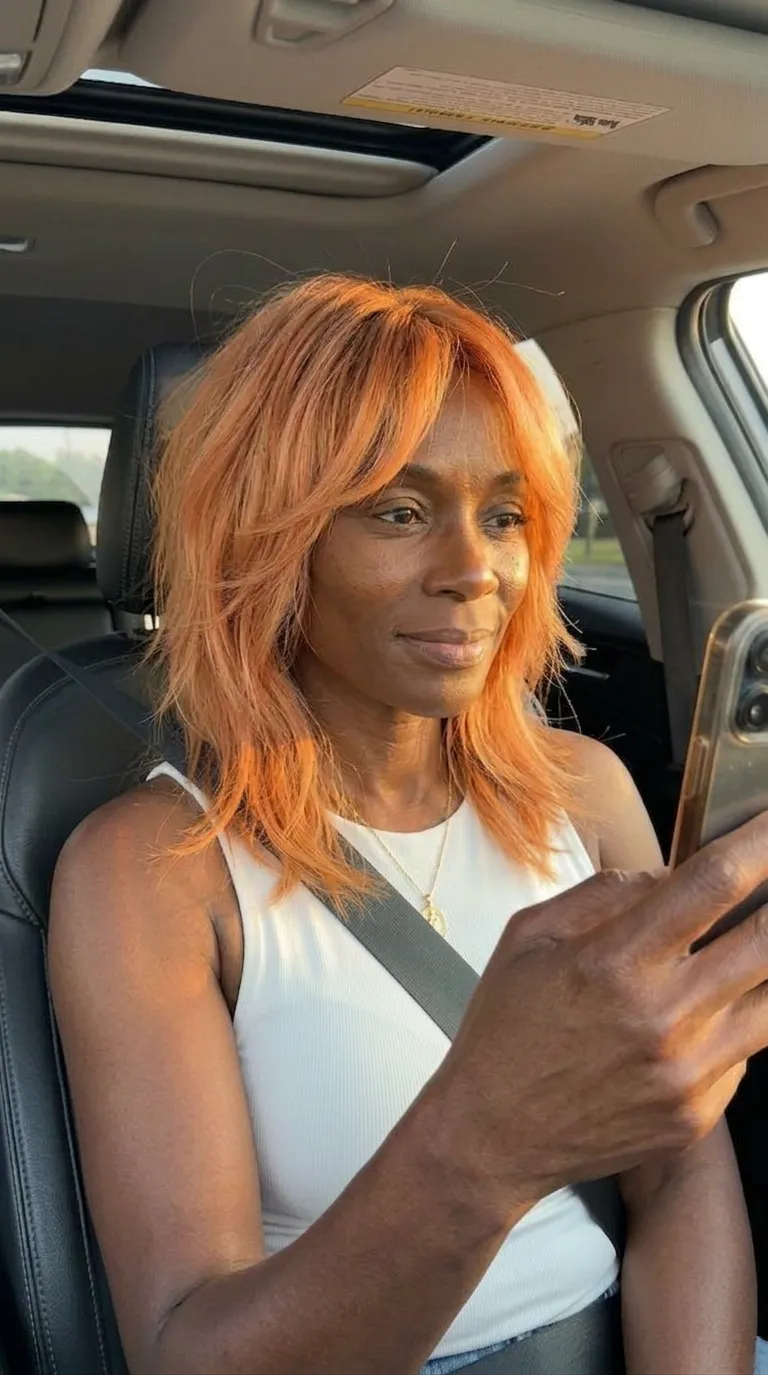 Vivid copper layered shag haircut with airy movement, soft fringe, and sunlit car-selfie mood for a bold summer 2026 refresh for women over 40