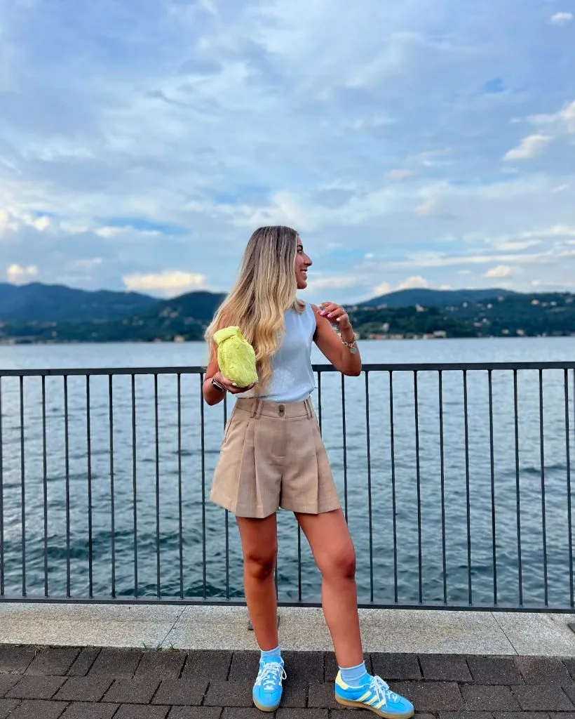 August Outfits 2026 White Tee and Tan Pleated Shorts With Neon Bag Pop