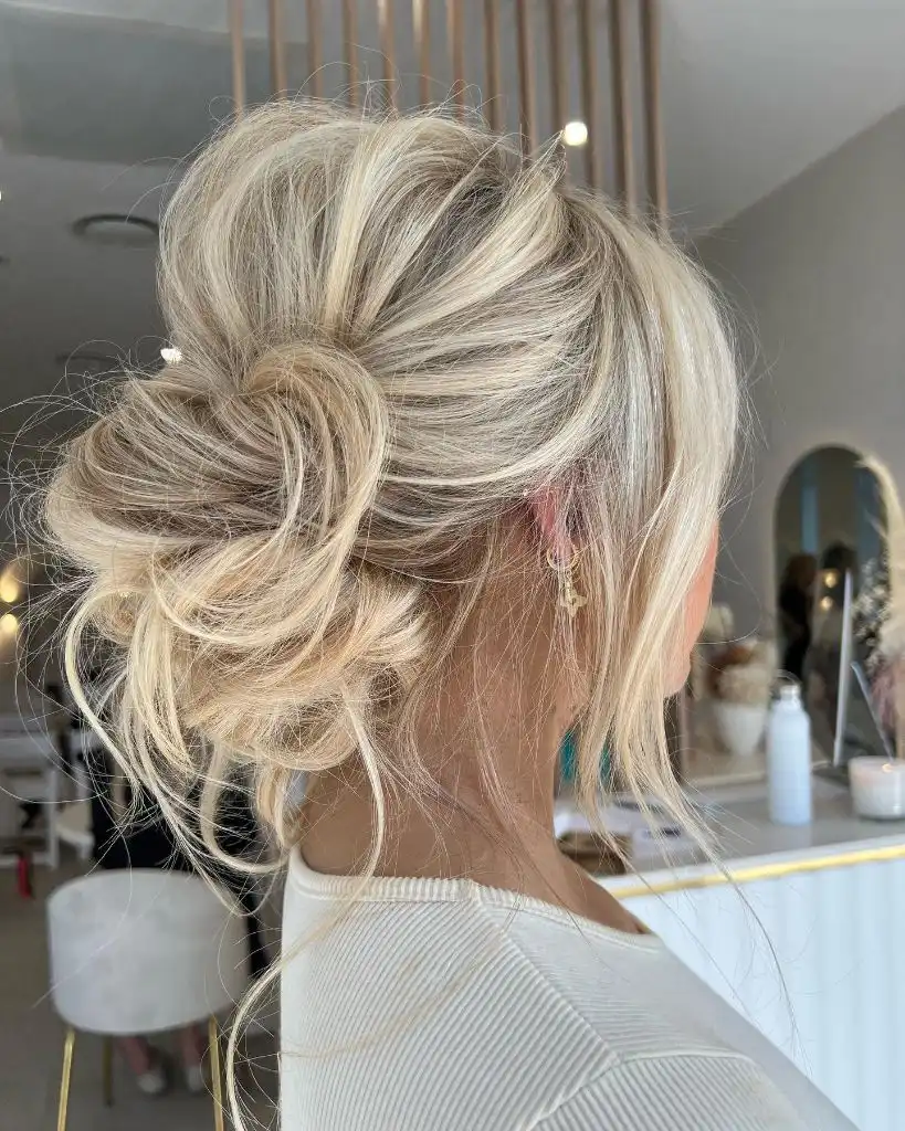 Fall Hairstyles for Wedding Guests 2026 Effortless Blonde Messy Bun with Wispy Face-Framing Pieces