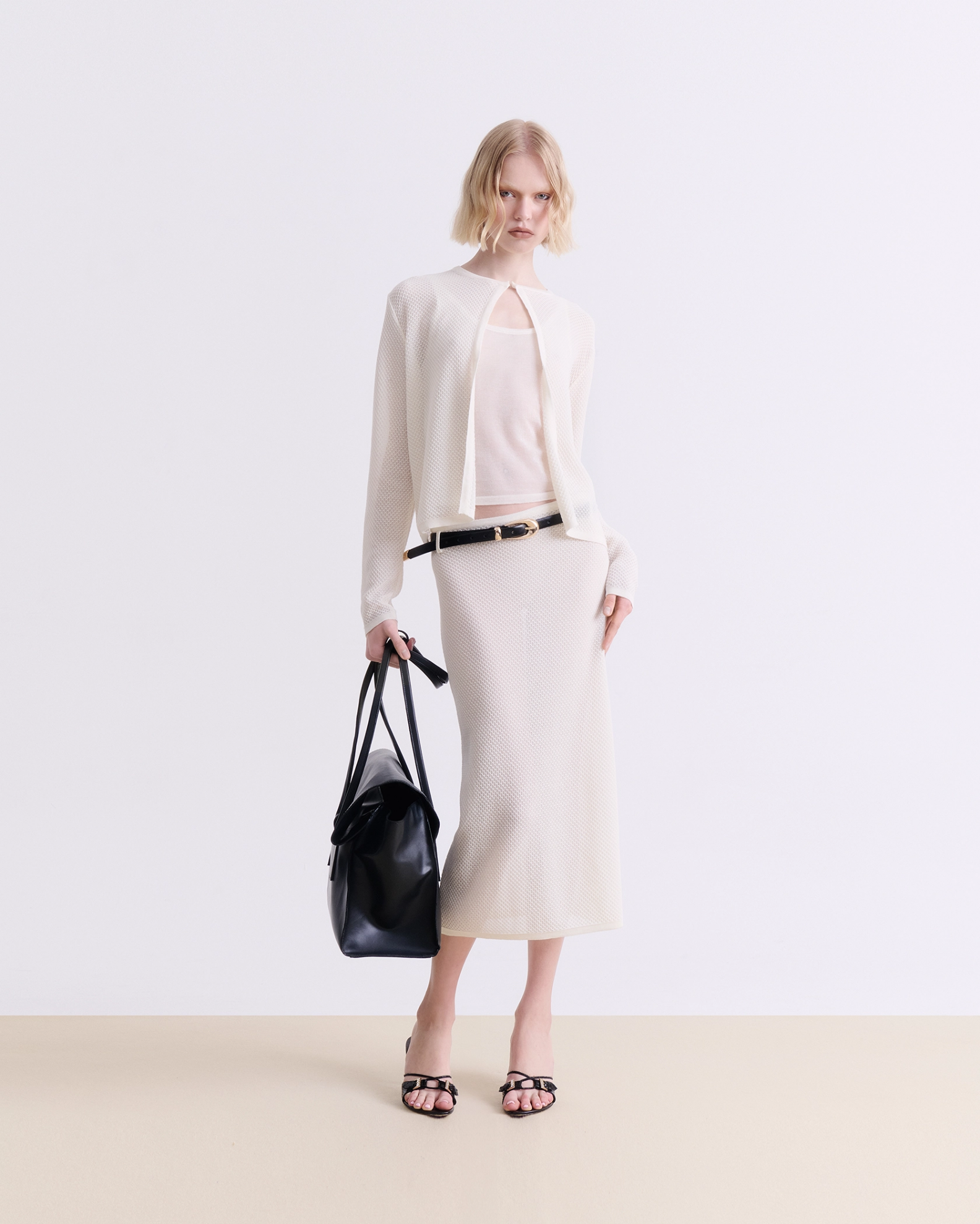 Woman wearing a cream knit midi skirt with a light cardigan and camisole