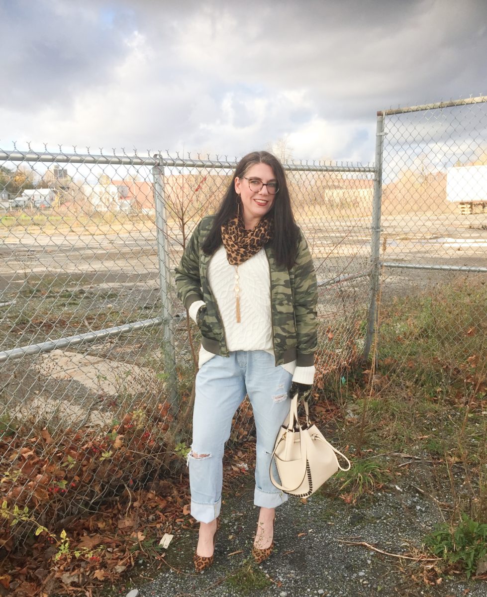 Woman wearing a cream sweater with a camouflage bomber jacket, boyfriend jeans and leopard pumps