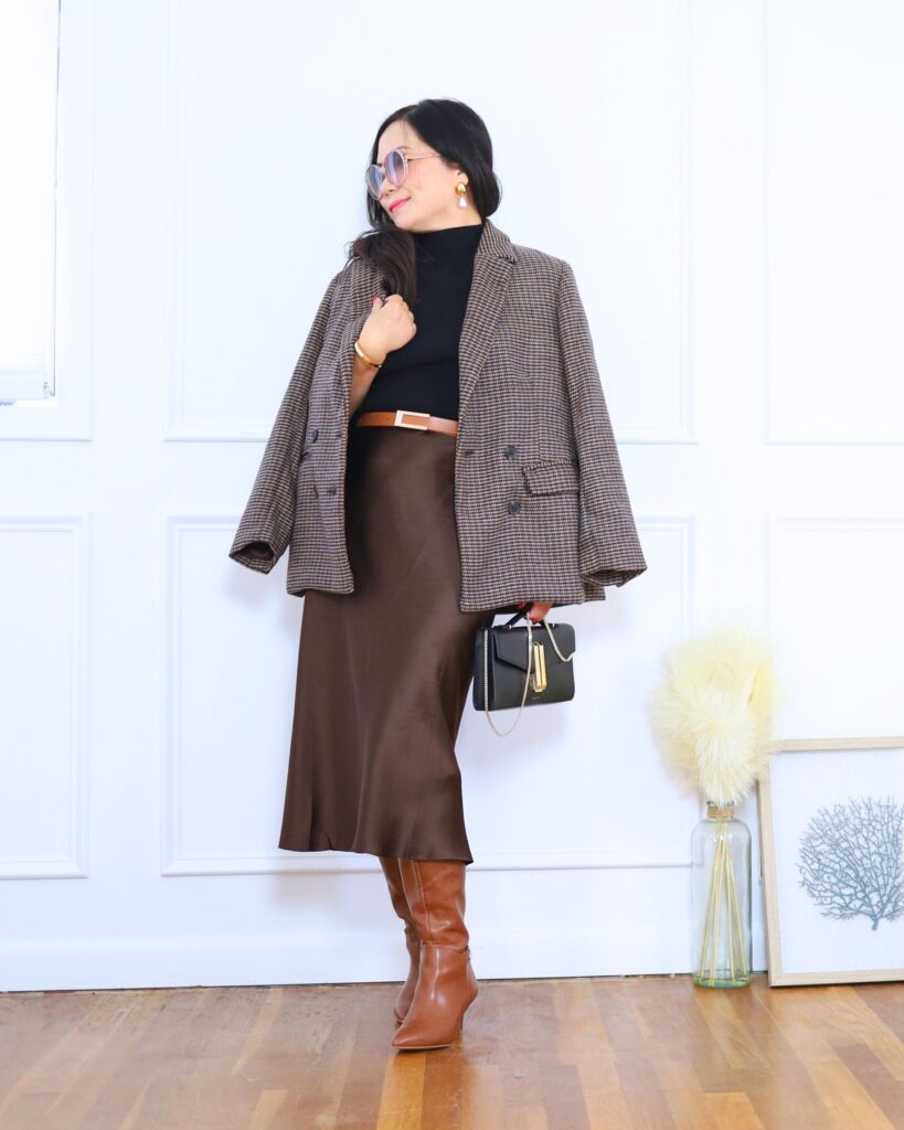 Checked blazer draped over shoulders with a brown satin midi skirt