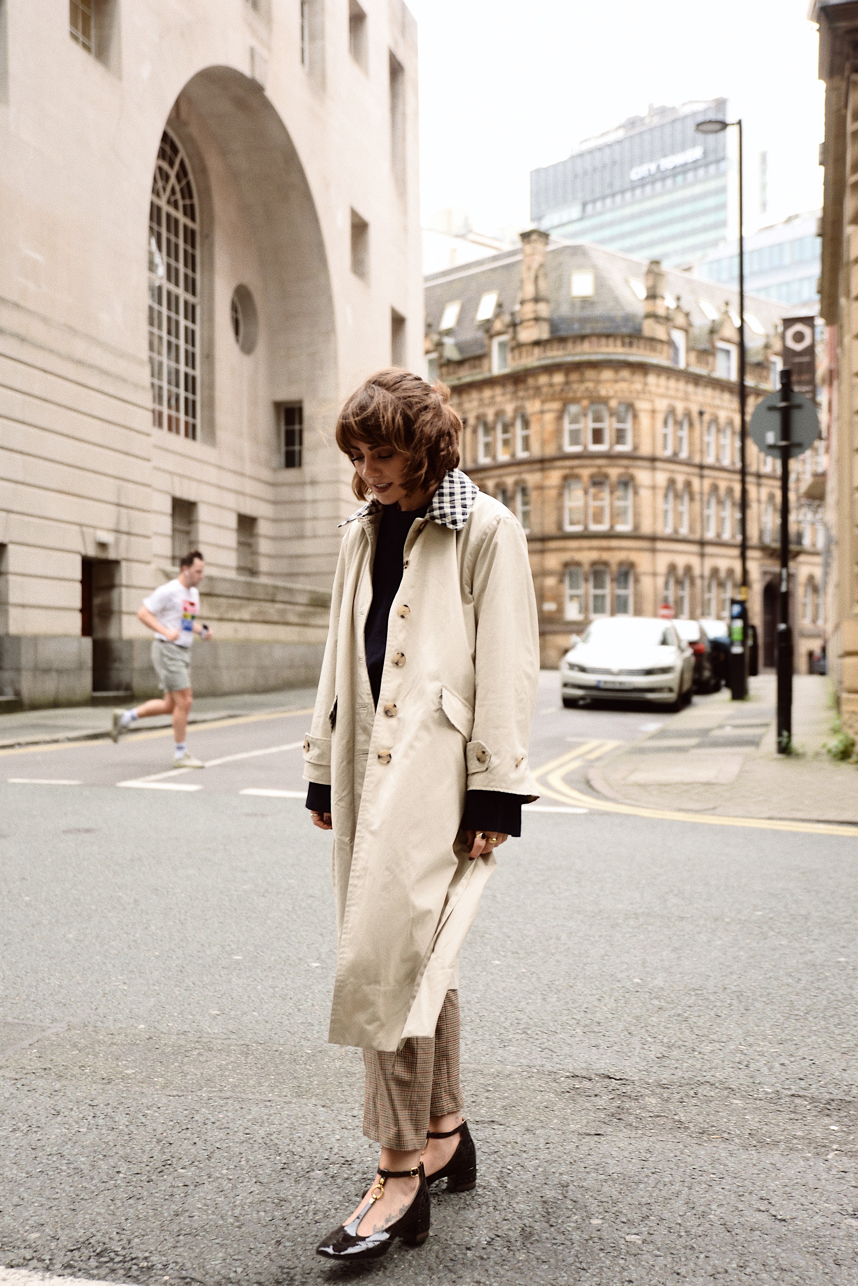 Woman wearing a long cream trench coat over dark layers on a city street
