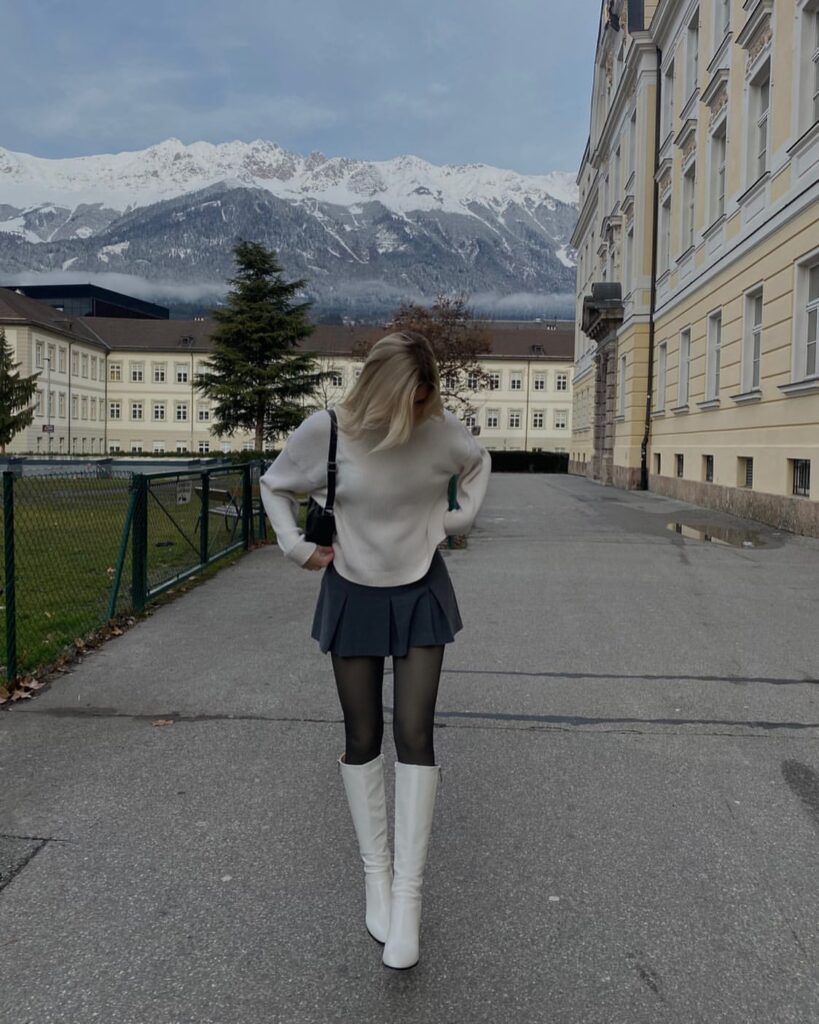 Cream sweater with grey pleated skirt and white knee-high boots