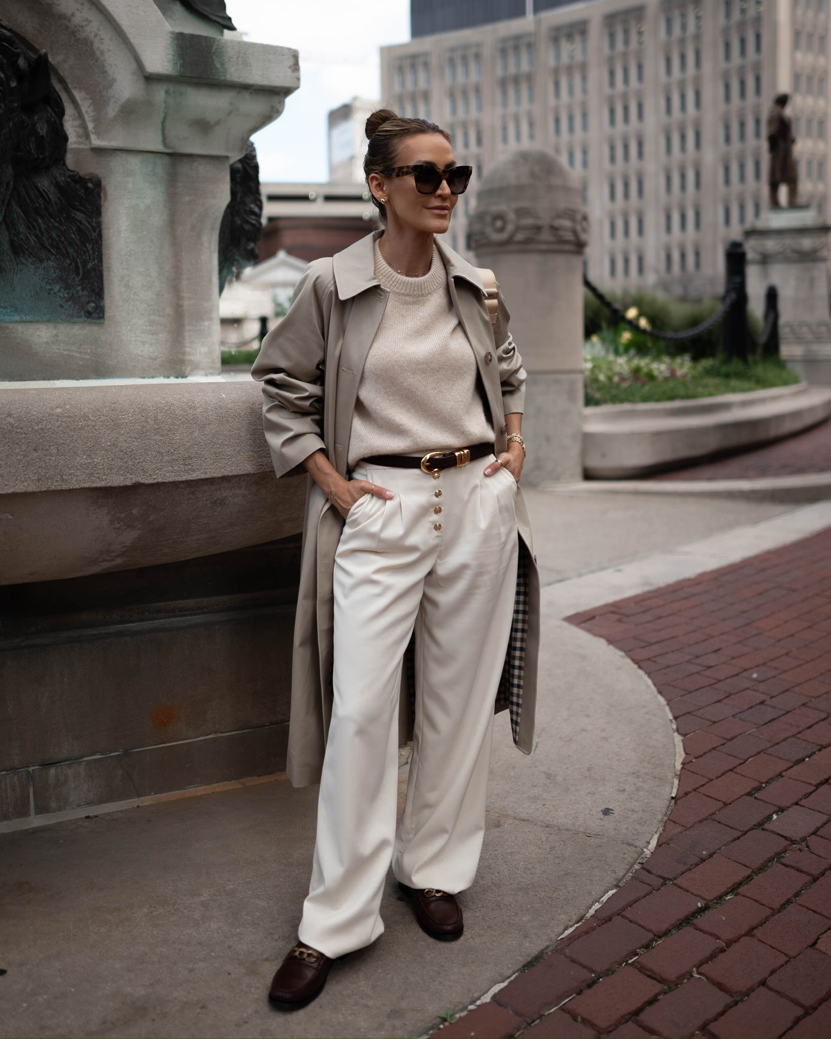 Woman in a grey trench coat with a cream sweater and wide white trousers