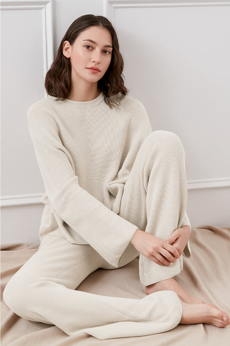 Woman wearing a soft cream knit lounge set sitting on a bed