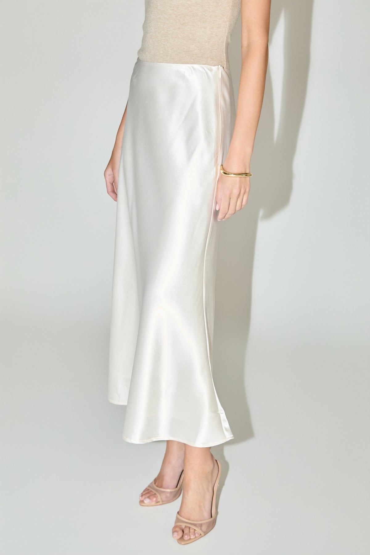 Woman wearing a long cream satin midi skirt with a beige knit top