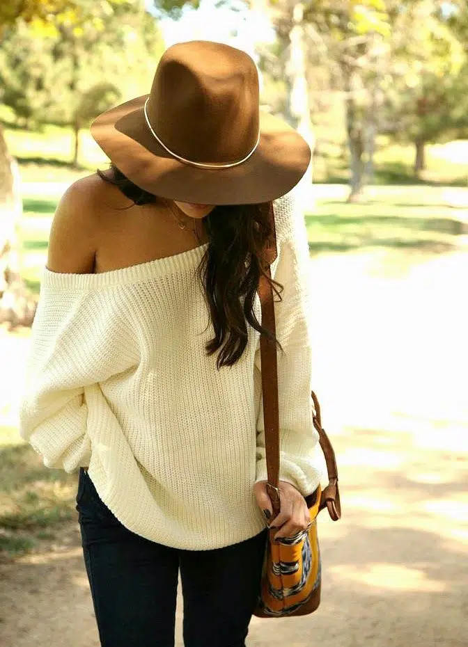 Off-the-shoulder white sweater with dark jeans and a wide-brim hat