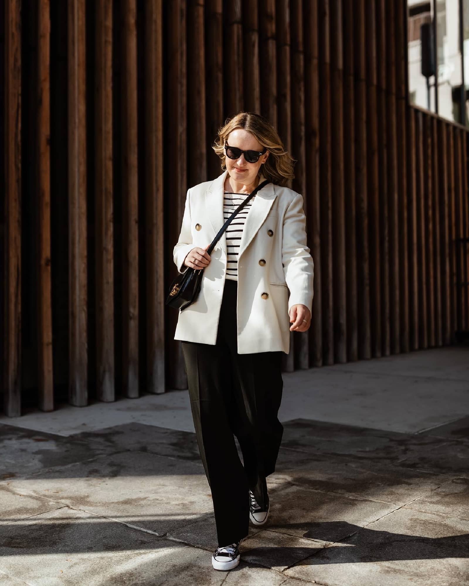 Woman wearing an oversized blazer, striped tee and black trousers with sneakers LA outfit