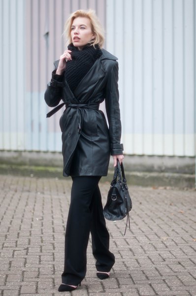 Belted black leather trench coat worn with a black sweater, scarf and wide trousers